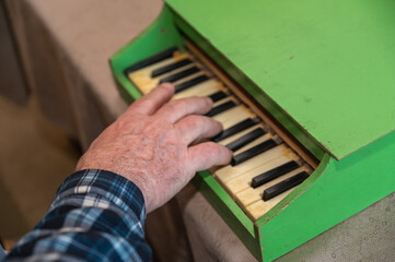 An elderly man plays a toy piano. His right hand is playing a jolly tune on an old children's...