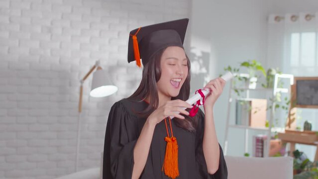 An Asian girl shows her certificate. She is greetings on her graduation ceremony. She is extremely happy on her successful and  achievement moment. She is so lively on her gown and obviously cheerful.