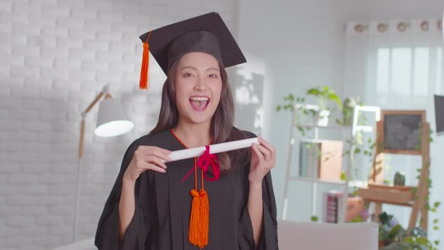 An Asian girl shows her certificate. She is greetings on her graduation ceremony. She is extremely happy on her successful and  achievement moment. She is so lively on her gown and obviously cheerful.