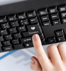 charity and technology concept - close up of female hand pressing donation button with heart on keyboard