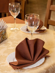 Close-up of a romantic serving in a restaurant, a table with a golden tablecloth, brown napkins and dishes, festive gold tinting, vertical
