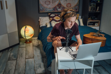 Home sound studio young teenager portrait using laptop computer and Headphones, playing guitar and recording voice music with microphone in the kid's room. Audio recording technology concept image