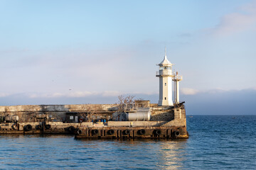 Fototapeta na wymiar Scenic cityscape view old ancient white lighthouse building on stone pier at Yalta Crimean harbor on Black sea on warm sunny day. Bay nautical beacon house tower