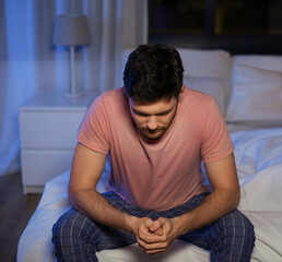 sleep disorder, insomnia and mental health problems concept - unhappy man in pajamas sitting on bed at night