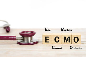 Concept word 'ECMO, Extra Corporeal Membrane Oxygenation' written on wooden blocks and stethoscope on the table. Copy space, medical concept.