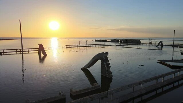 Peaceful sunset view of abandoned villa epecuen, popular freshwater pool spa overfilled with salty flood water, aerial pan shot capturing ruins of poolside slides and railing.