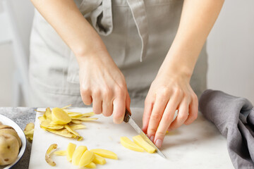 Obraz na płótnie Canvas Hands cut potatoes on marble board. Woman in apron cut potato. Food preparing. Potatoes cubes