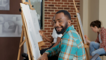 Portrait of young man drawing inspiration object in art class using pencil, canvas and easel to develop artistic skills. Leisure activity to learn to draw sketch for development. Handheld shot