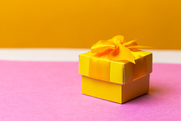 Closeup Image Of Wrapped Christmas and New Year Gift in Yellow Paper Tiny Box Placed Over Pink and Yellow Background.