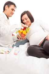 Obraz na płótnie Canvas Pregnancy Concepts. Portrait of Husband Man Offering His Pregnant Wife Fresh Vegetables on Glass Bowl Over White Background.