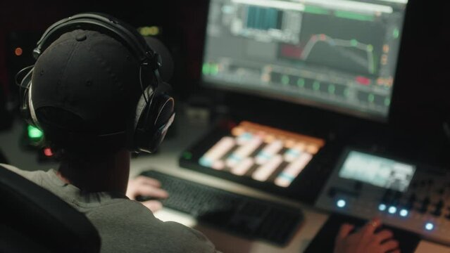 Sound engineer seen seated from behind uses the computer to mix audio music
