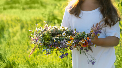 wreath of meadow flowers in hands girl, summer natural background. floral traditional decor for...