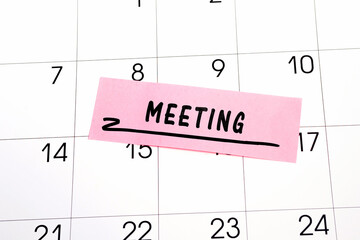 The word Meeting written on a pink sticky note posted on a calendar or planner page. Closeup of a personal agenda