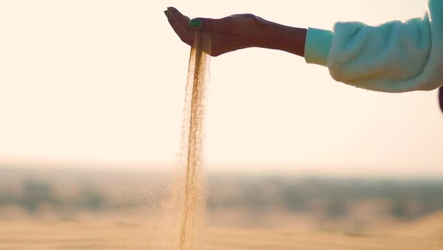 Slow motion shot of hands of an Indian female pouring sand of the Thar desert at Sam Sand dunes in Jaisalmer, Rajasthan, India. Female pouring sand in the desert. Desert Travel background. 