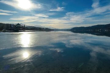 View on Woerthersee in Poertschach in Carinthia, Austria.The calm surface of the lake is reflecting the mountains, sunbeams and clouds. Clear and sunny day. Karawanks mountain range. Alps, Lake Woerth