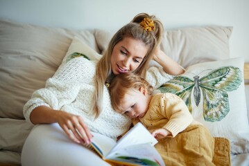 Young beautiful mother reading her baby daughter at home.