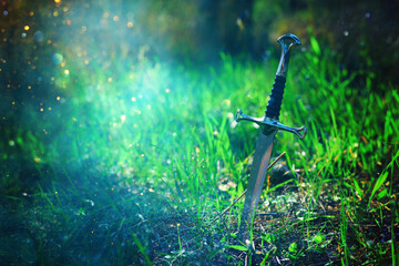 mysterious and magical photo of silver sword in the England woods and light flare. Medieval period...