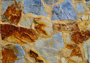 A section of a multi-coloured ocre, orange, yellow, red and blue stone wall in southern Spain - for background and texture use.