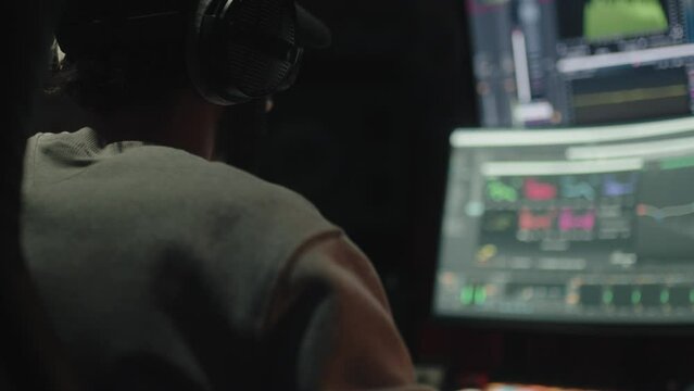 Sound engineer seen seated from behind uses the computer to mix audio music