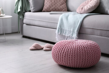 Pink knitted pouf near sofa in living room. Space for text