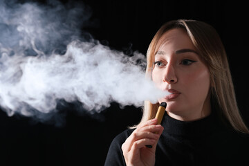 Obraz premium Young woman using electronic cigarette on black background