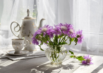 A bouquet of cornflowers and coffee on a sunny window on a summer day