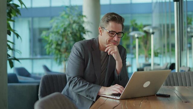 Businessman using laptop computer in office lobby or on cafe terrace. Happy middle aged man, entrepreneur, small business owner working online.
