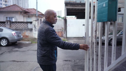 An older man leaving house in the drizzle opening entrance door and going out to street