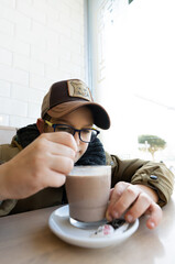 CLOSE-UP OF A BLOND BOY WITH GLASSES AND CAP SPOONING BREAKFAST.