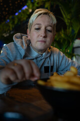 SHORT-HAIRED BLONDE WOMAN LOOKS AT AN APPETIZER AND PICKS UP A POTATO