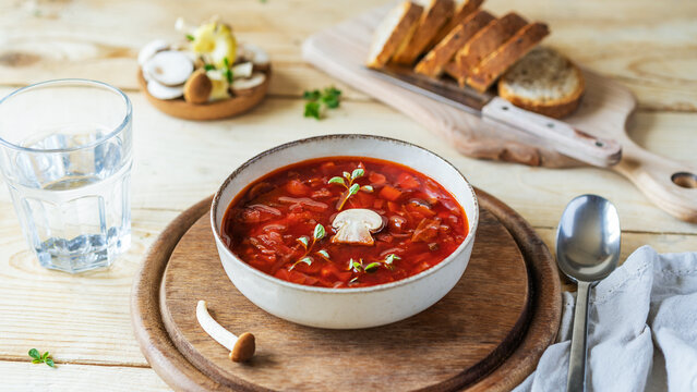 Vegan beetroot soup with mushrooms in a bowl, bread, glass of water on a wooden background