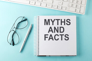 Keyboard, notebook,pen and glasses on the blue background , text MYTHS AND FACTS
