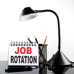 JOB ROTATION text on notebook with pen and table lamp on the black background