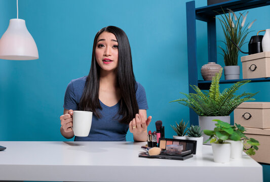 Portrait of social media influencer filming beauty podcast talking with remote subscribers during live video in studio with blue background. Attractive content creator recording cosmetics vlog