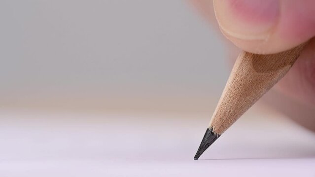 Macro of pencil writing or drawing. Unknown person drawing line or letter on white paper.