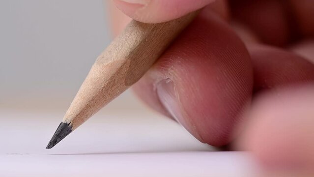 Macro of pencil writing or drawing. Unknown person drawing line or letter on white paper.