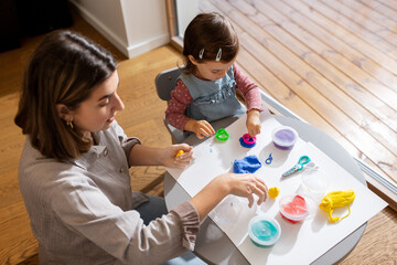 family, creativity and craft concept - mother and little daughter playing with modeling clay at home