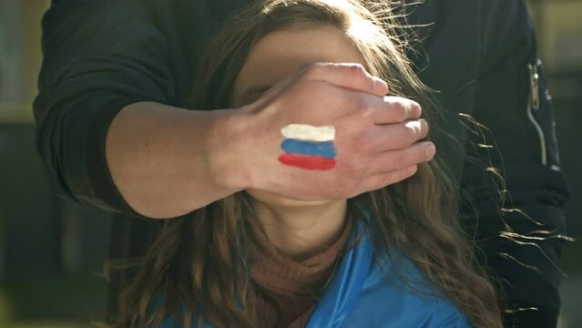 Man's hand with the image of the Russian flag roughly closes the face of a little girl with the Ukrainian flag. Freedom for Ukraine. Russian aggression.