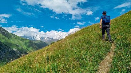 Fototapeta na wymiar A male backpacker on a hiking trail to Chubedishi viewpoint. There is an amazing view on the Shkhara Glacier,near the village Ushguli the Greater Caucasus Mountain Range in Georgia, Svaneti Region