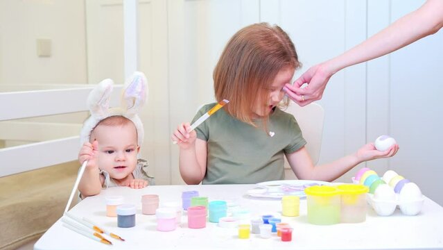 A four year old girl was painting with paints and her nose itched. Mom's hand scratches her daughter's nose. Young children are preparing for the Easter holiday at home.