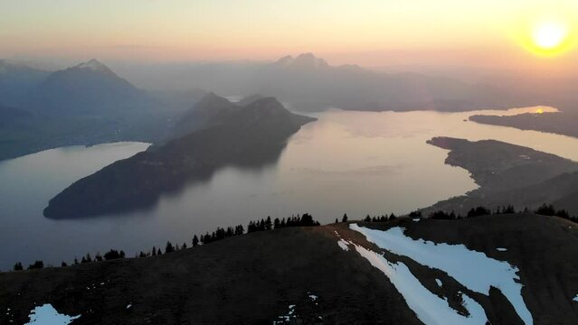 Aerial flyover over the peaks of the Alps near Rigi, Switzerland with a view of Lake Lucerne (Vierwaldstattersee) during a  a golden sunset at the beginning of spring with snow melting