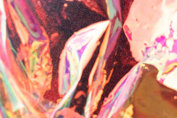 Blurred holographic background. Defocused multicolored texture of wrinkled foil in red colors.