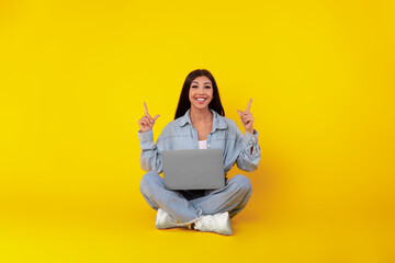Happy lady using laptop pointing up at studio