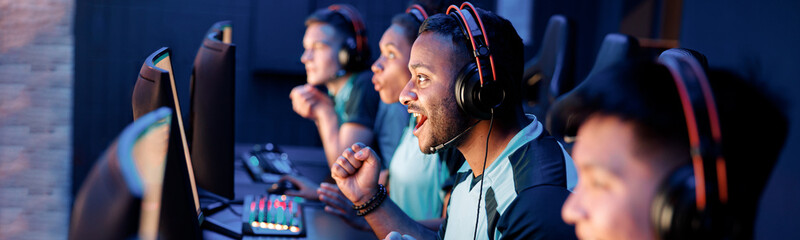 Team of professional esport gamers with happy man in focus playing in video games on cyber games tournament indoors