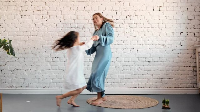 Active young mom babysiter and cute little kid daughter jumping dancing in modern house living room, happy family mother with child girl having fun enjoy playing funny activity together at home