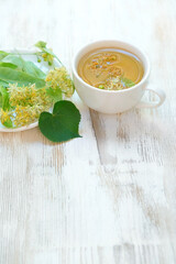 glass cup with linden tea and fresh green leaves on white wooden table. Medicinal plant, flowers used for herbal teas and tinctures. folk alternative traditional medicine remedy