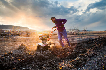 organic farming man cultivates the ground at sunset with a tiller  preparing the soil for sowing