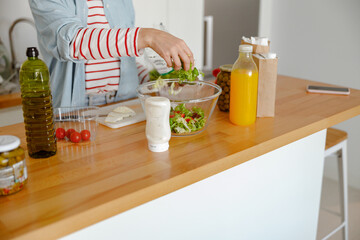 Close up of woman standing by kitchen counter and adding ingredient in bowl while making delicious...