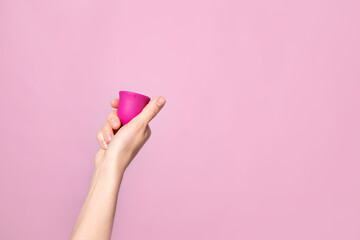 Mature content A young woman folding a pink menstrual cup in her hand. Pink colored background. Space for text. Eco-friendly silicone women's health cycle