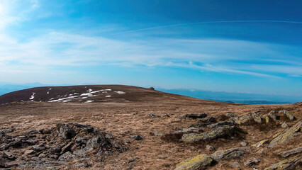 A vast, golden pasture on top of Sauofen, Austrian Alps. A lot of big stones on the grounds. High mountain chains in the back. Blue sky, with a few clouds. Outdoor activity. Serenity and calmness